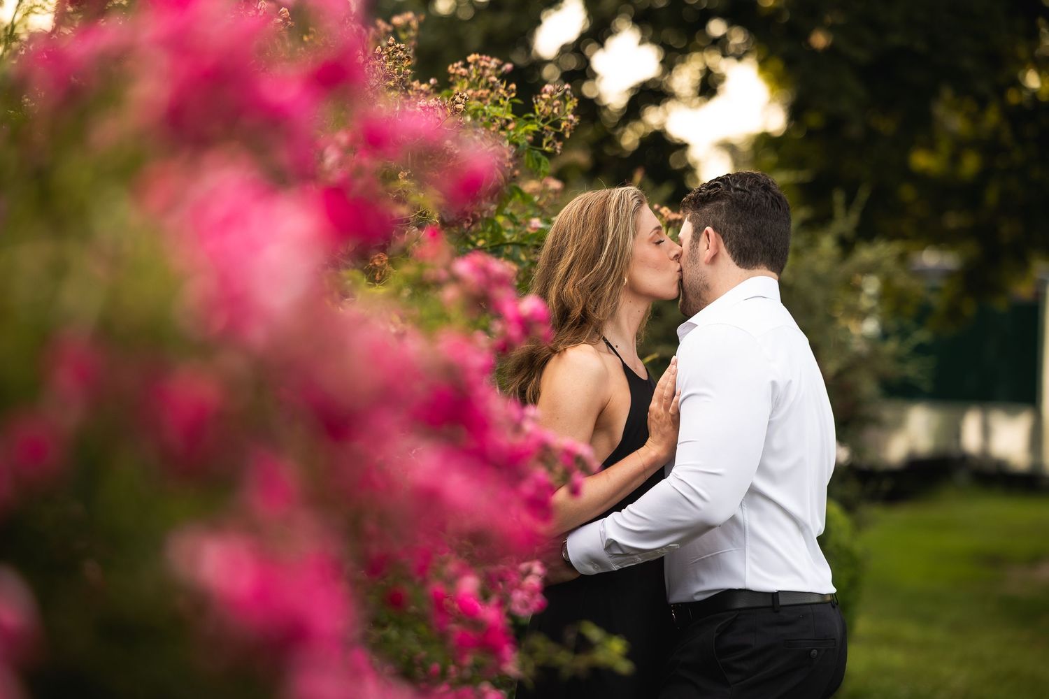 A couple embraces in a garden with vibrant pink flowers in the foreground creating a romantic atmosphere.