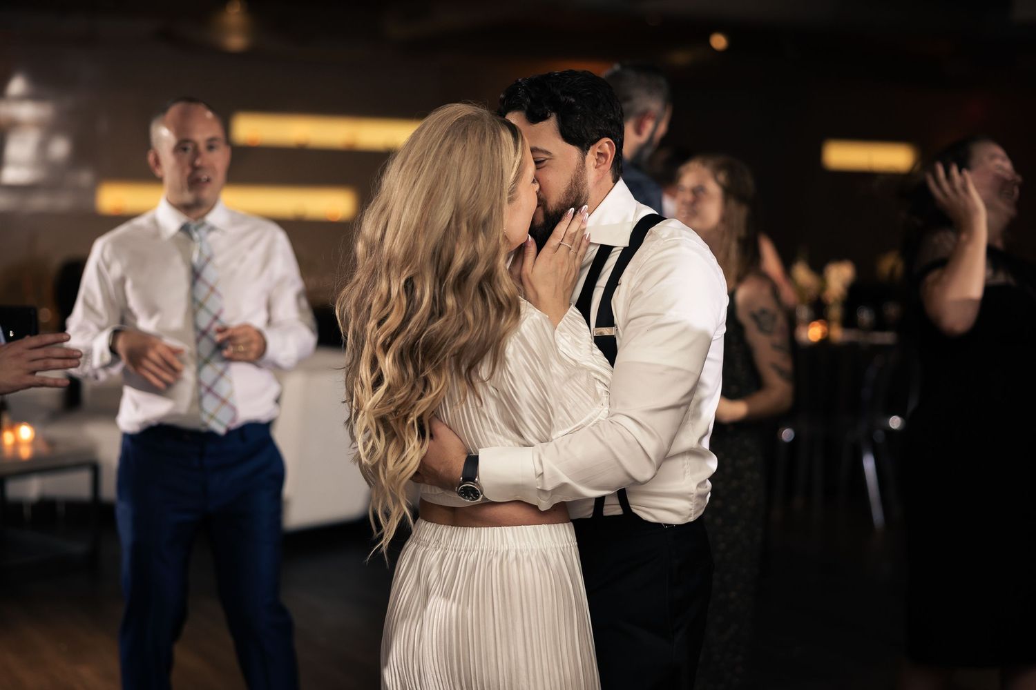 People dancing together at a dimly lit wedding reception with warm lighting and formal attire.
