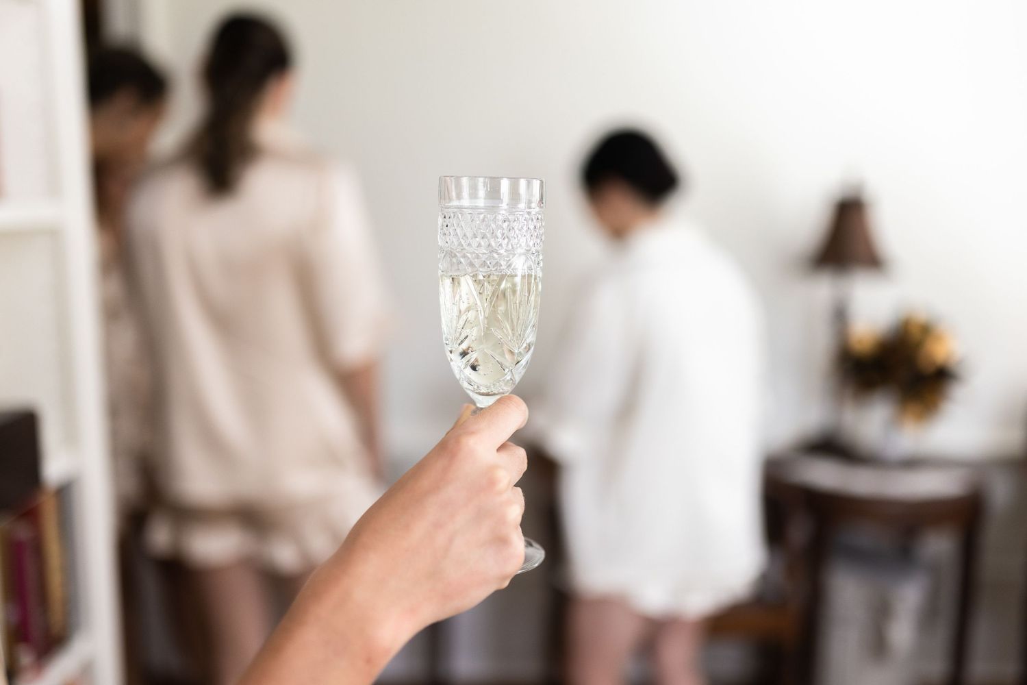 Hand holding up a champagne flute in celebration against a bright background.