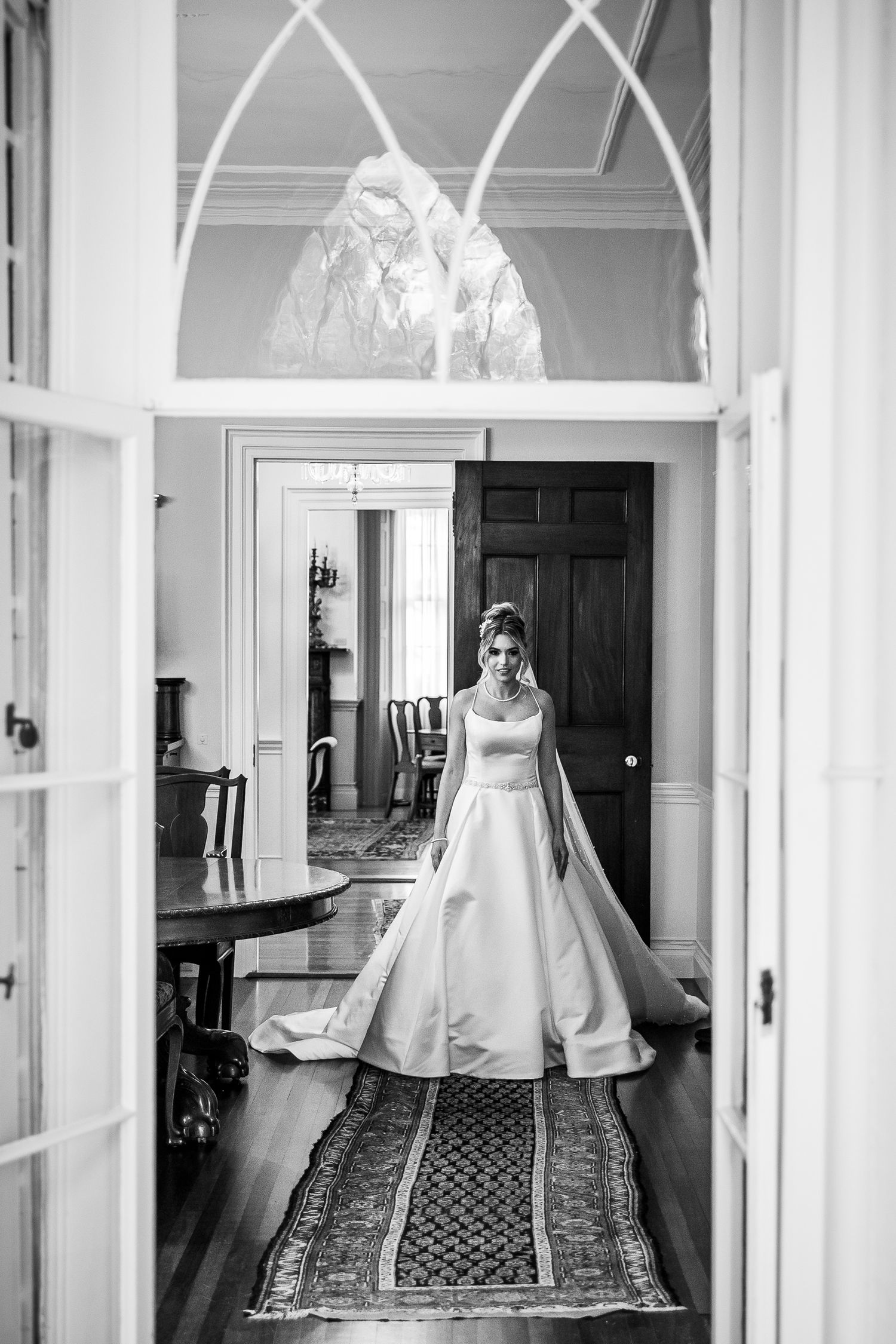 Wedding dress displayed in a grand hallway with ornate architectural details and patterned carpet.