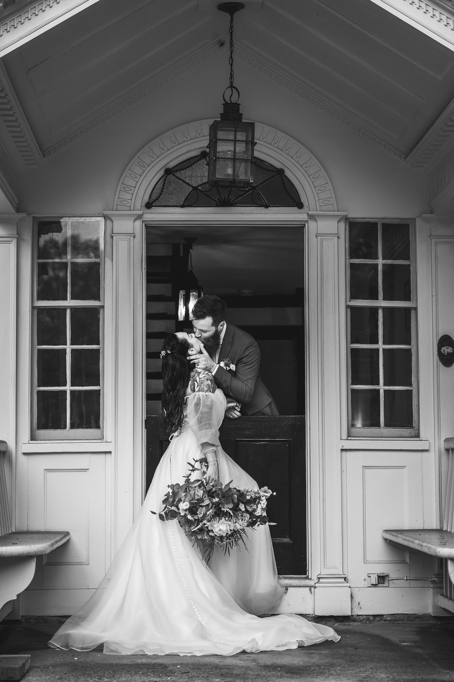 Classic black and white wedding portrait on an elegant white porch with architectural details.