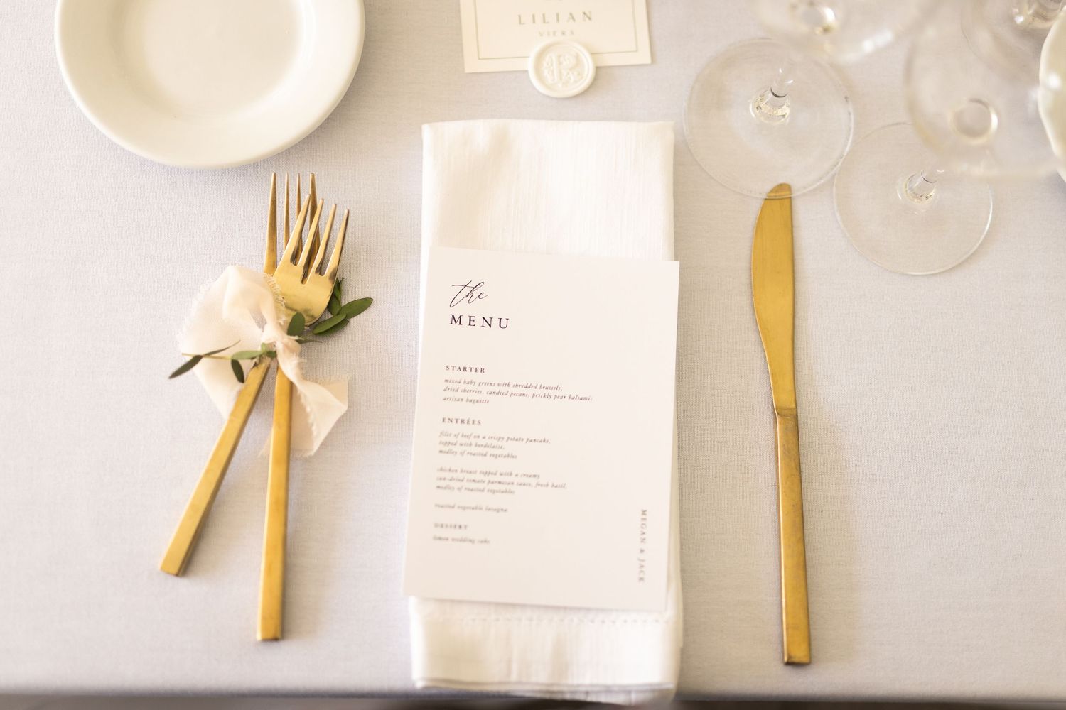 Minimalist wedding place setting with gold cutlery and white menu card.