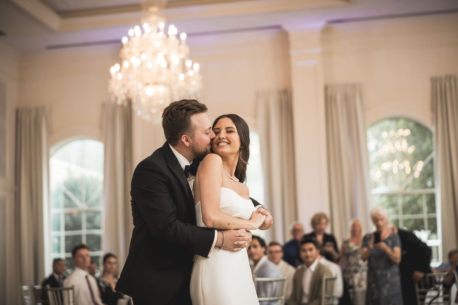 Couple shares an intimate dance moment under crystal chandeliers at their wedding reception.