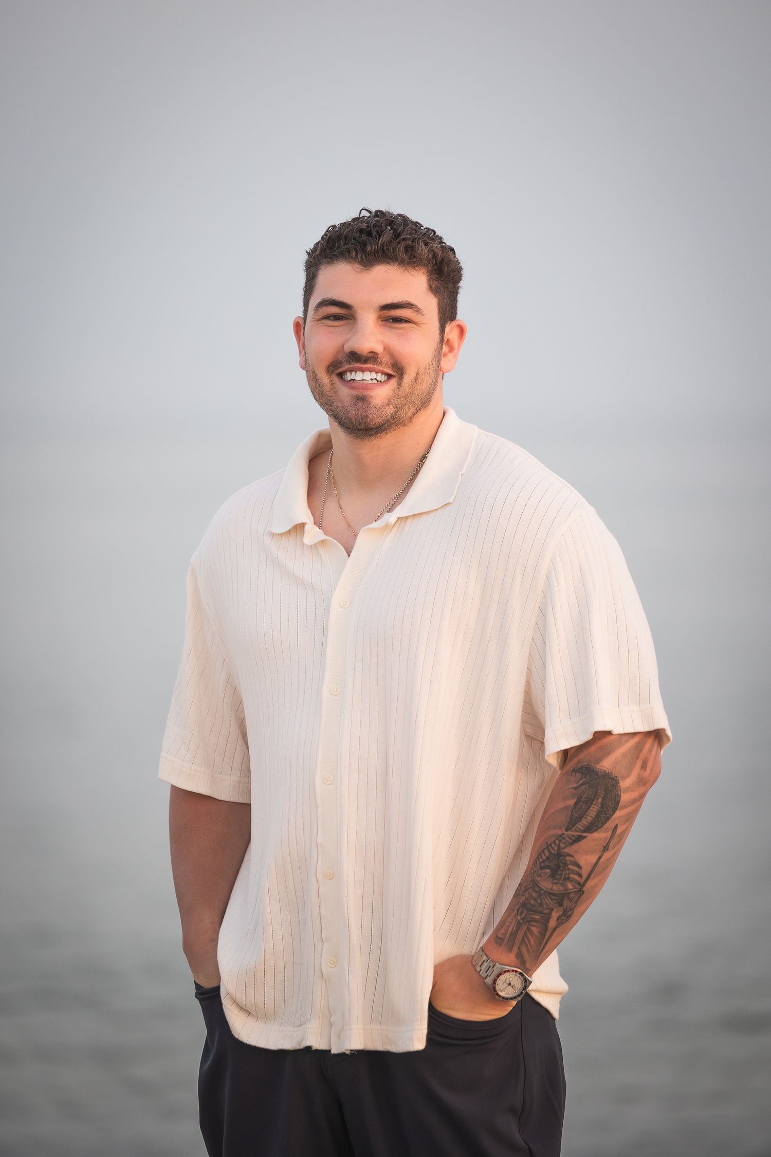 A person in a white short-sleeved shirt smiles while posing against a gray background.