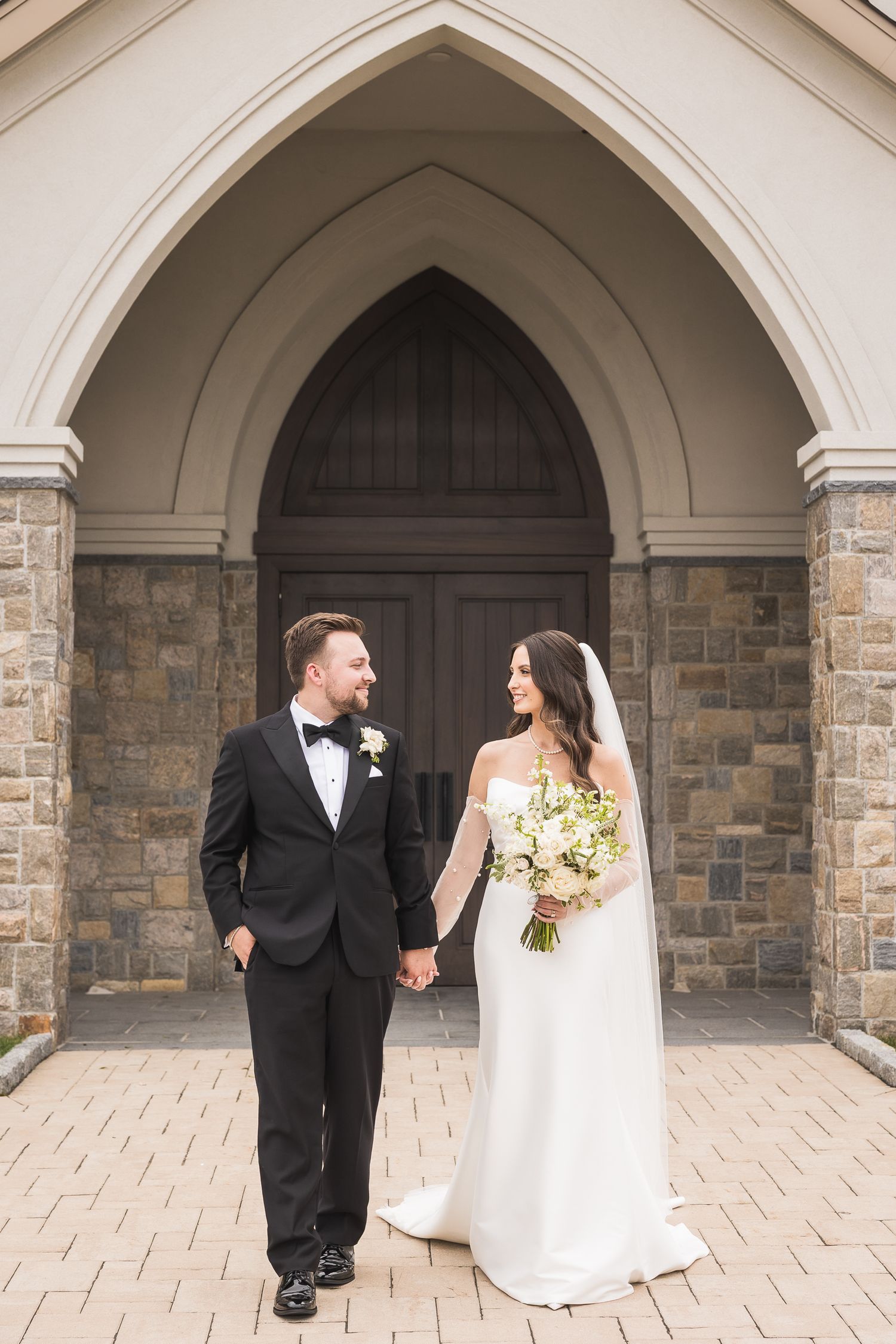 Wedding couple posing under gothic stone arches at elegant venue.