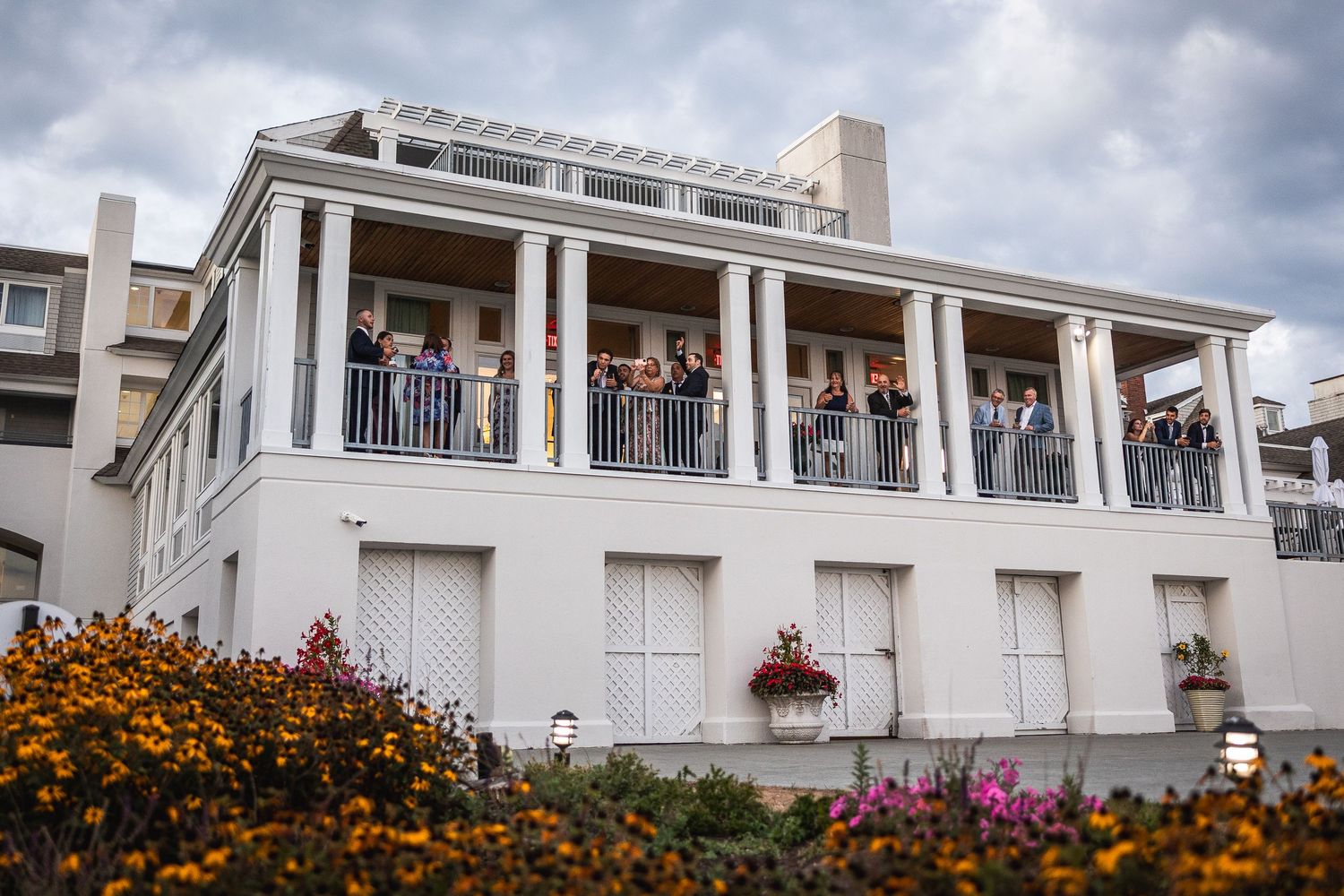 Panoramic view of a white columned wedding venue with colorful flowers and cloudy sky.