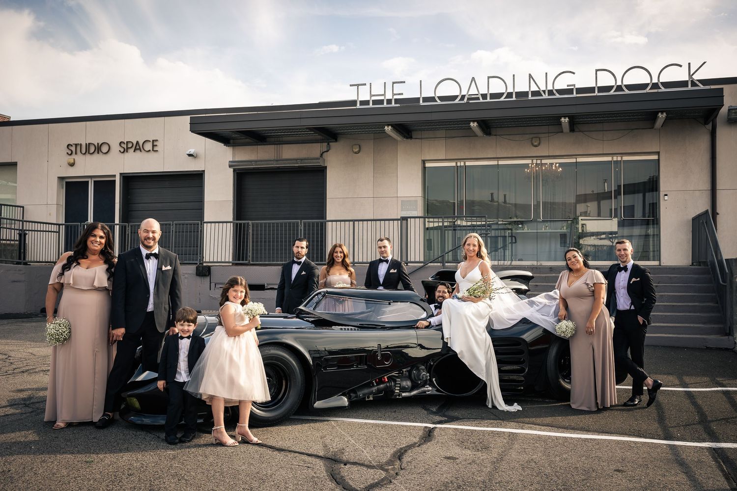 A wedding party poses in front of a loading dock at an industrial venue with an urban aesthetic.