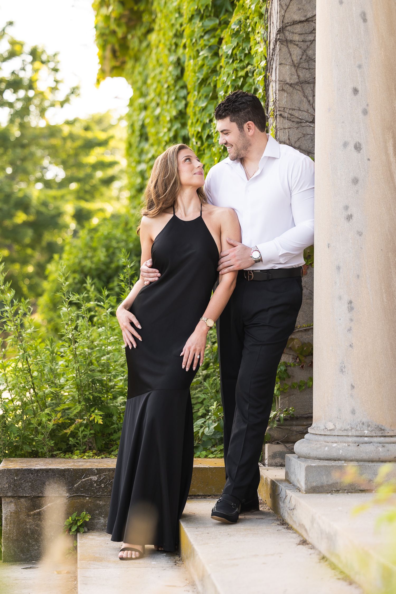 A couple shares romantic moments in a series of photos under stone columns in a garden setting.