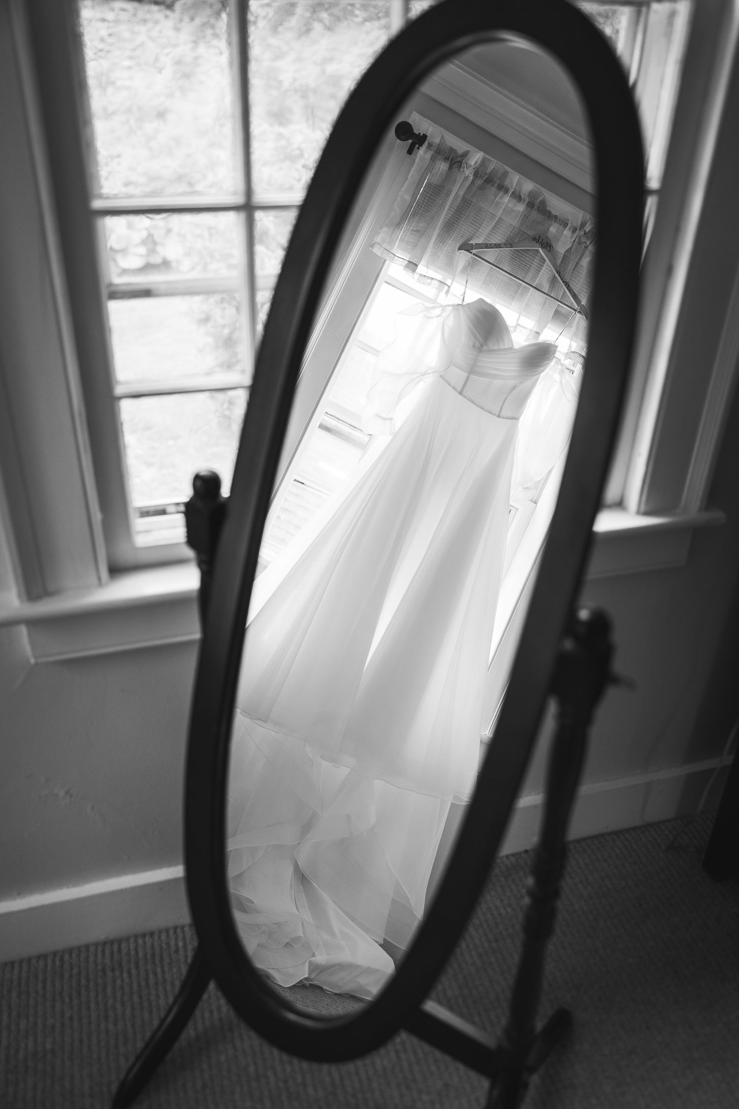 Wedding dress hanging in window light captured in black and white photography.