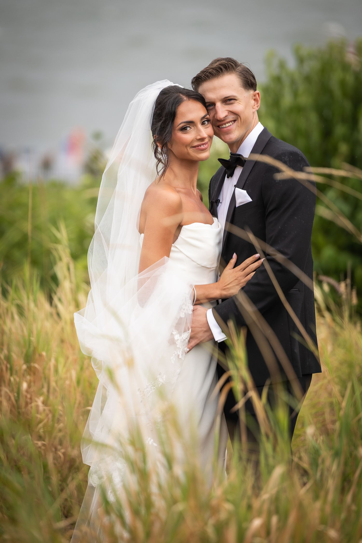 Couple shares intimate moment in tall grass during wedding photoshoot.