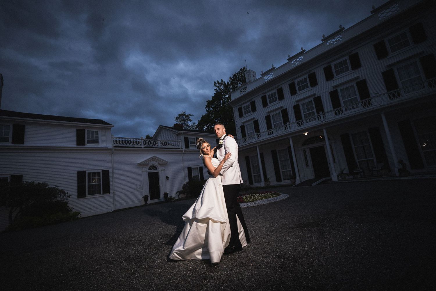 Dramatic evening wedding photos taken outside a colonial style building with moody lighting.