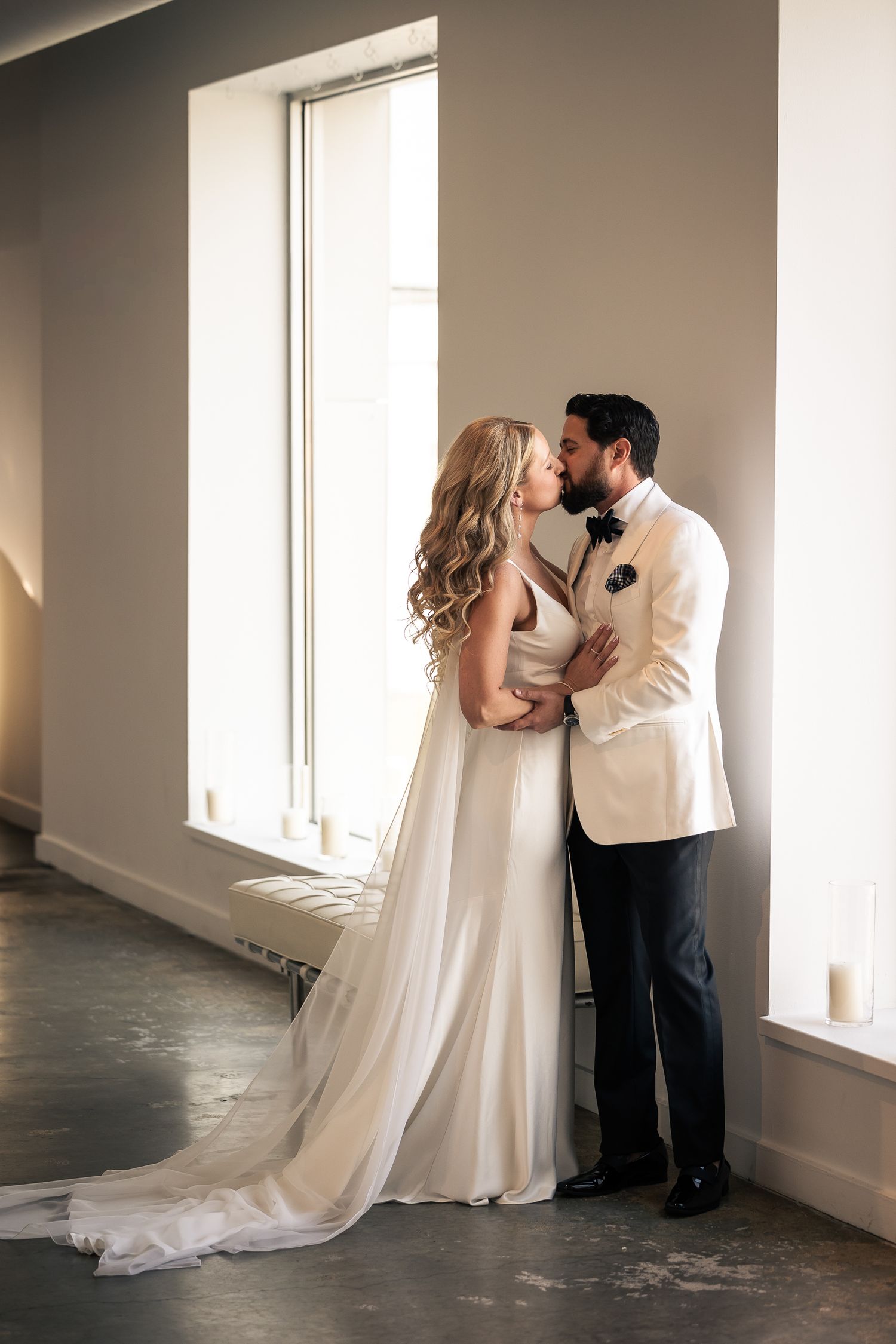 A romantic wedding couple shares intimate moments in a bright, minimalist room with natural window light.