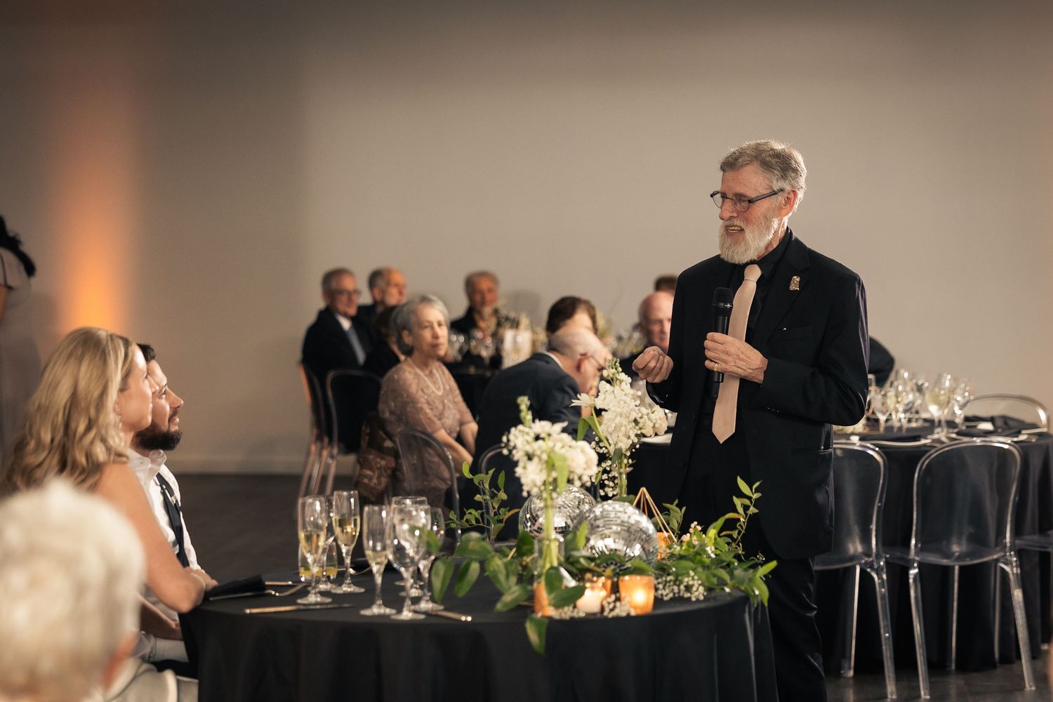 Elegant black and white wedding reception setup with round tables, floral centerpieces and soft lighting.
