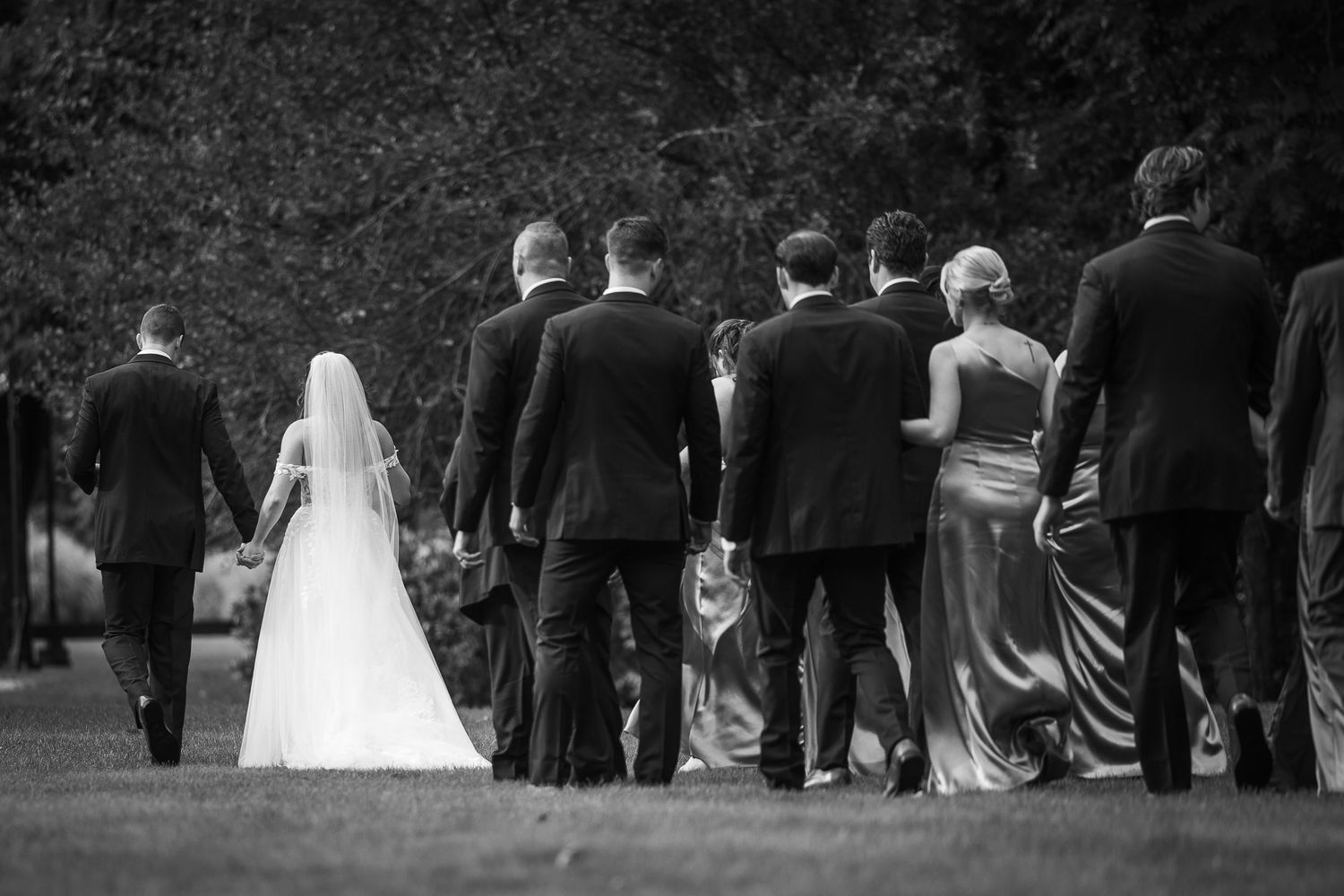 Wedding party walks away from camera through a garden path during an outdoor ceremony.