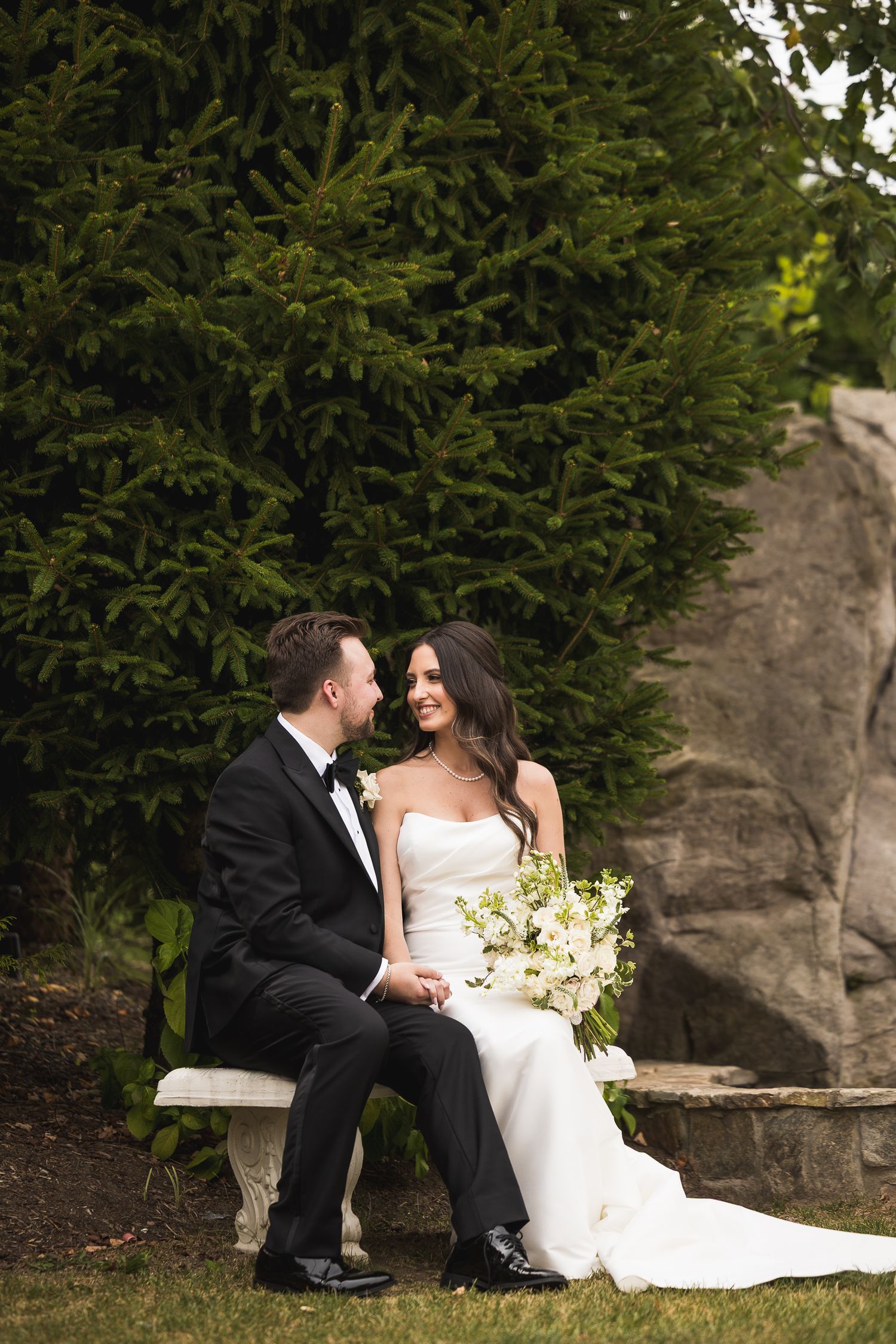 Wedding couple shares intimate moments while seated on stone steps surrounded by greenery.