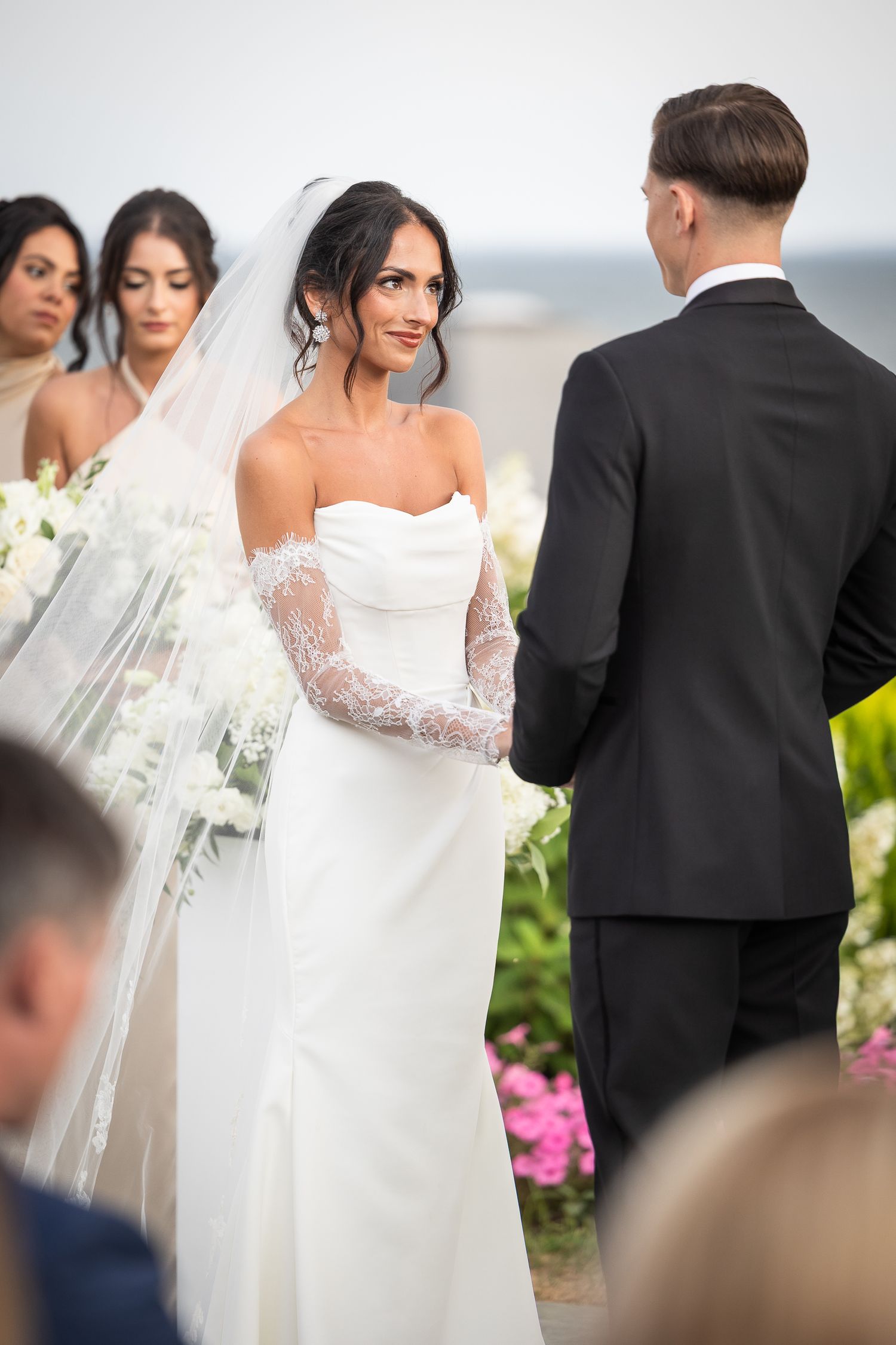 Elegant outdoor wedding ceremony with a bride in a strapless white gown and lace sleeves.