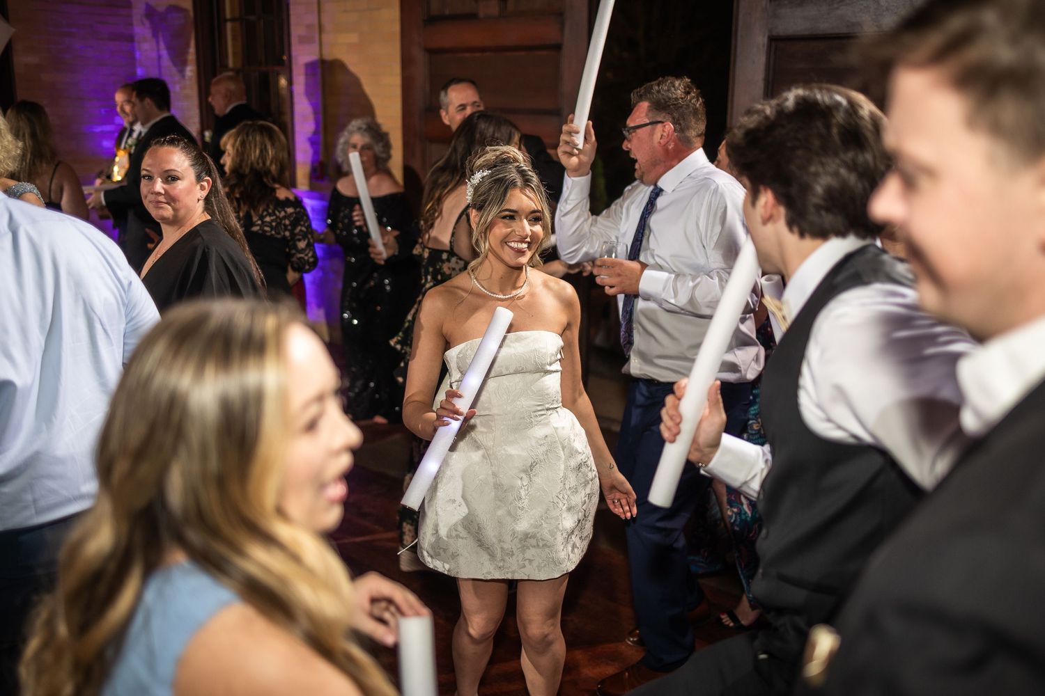 Wedding reception dance floor filled with guests celebrating under purple lighting.