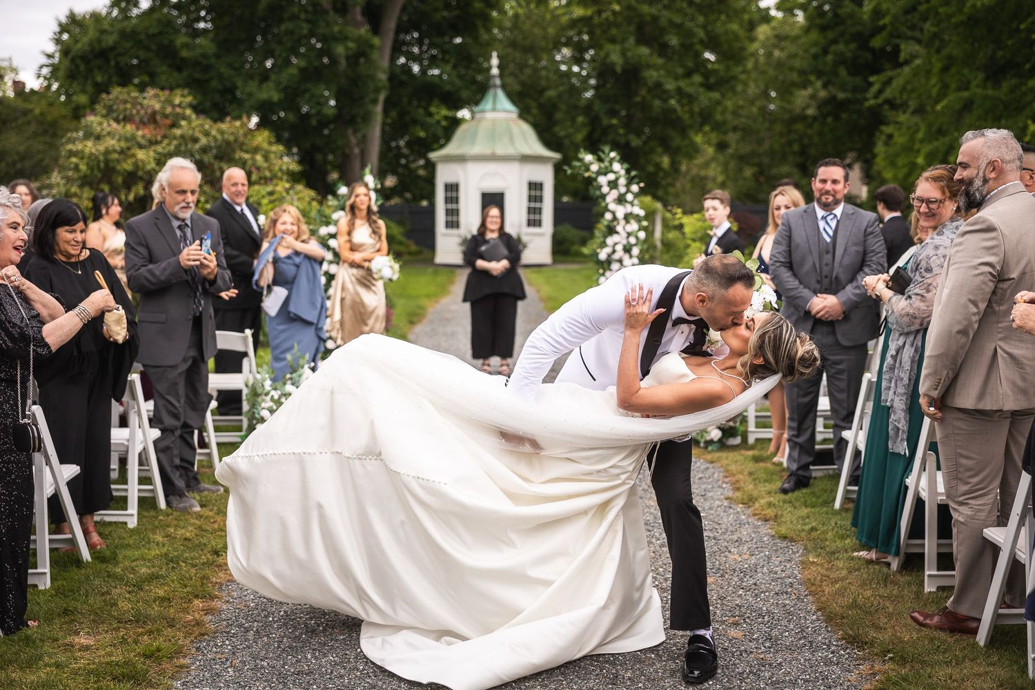 Wedding party and guests celebrating outdoors along a tree-lined path.