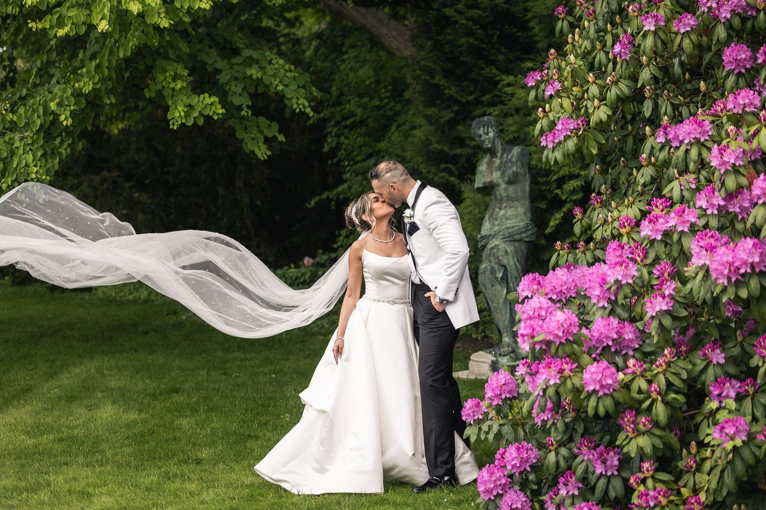 Garden wedding ceremony setup with flowing veil and pink azalea flowers in background.