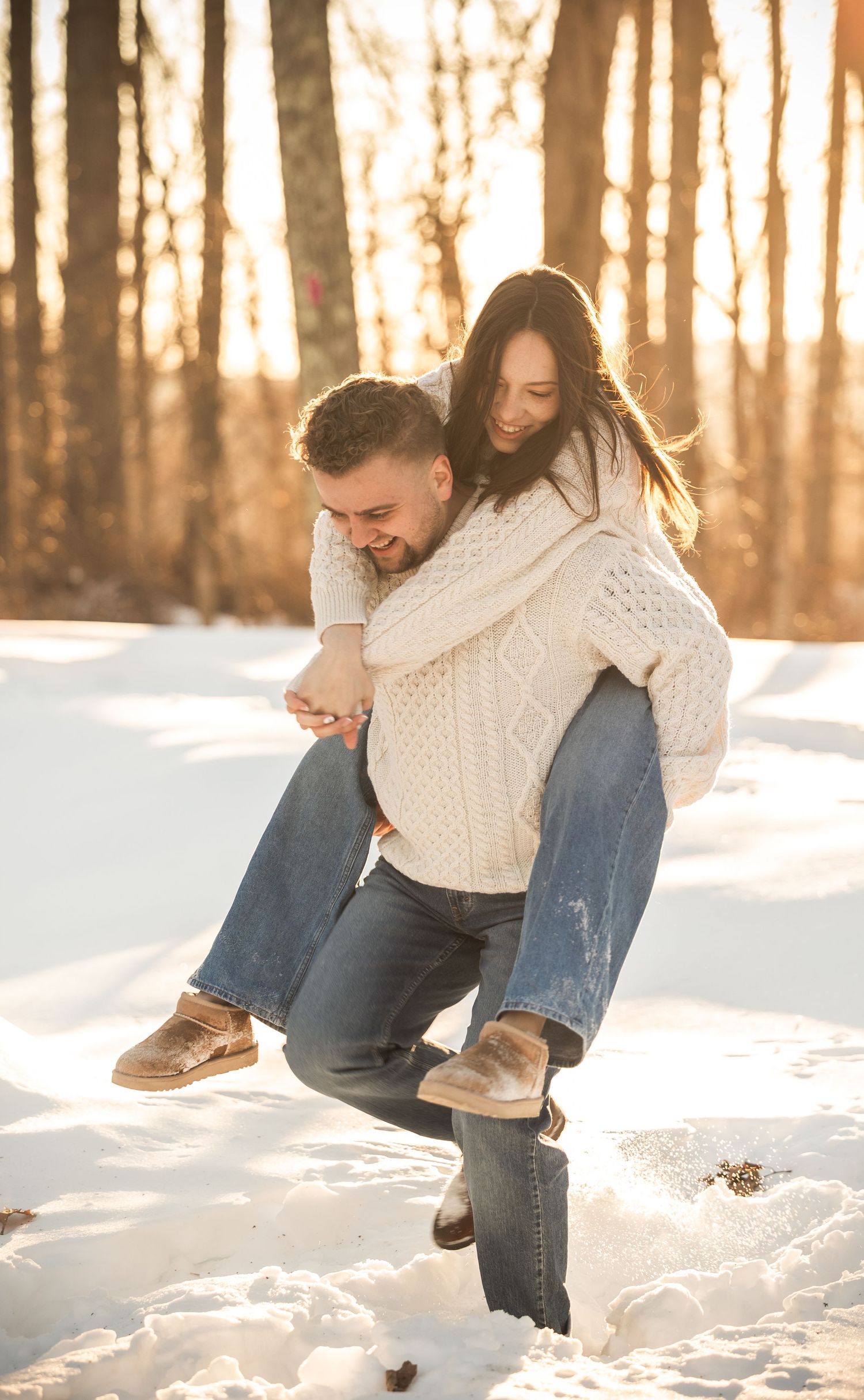 A couple sits together in snowy winter woods during sunset creating romantic silhouettes.