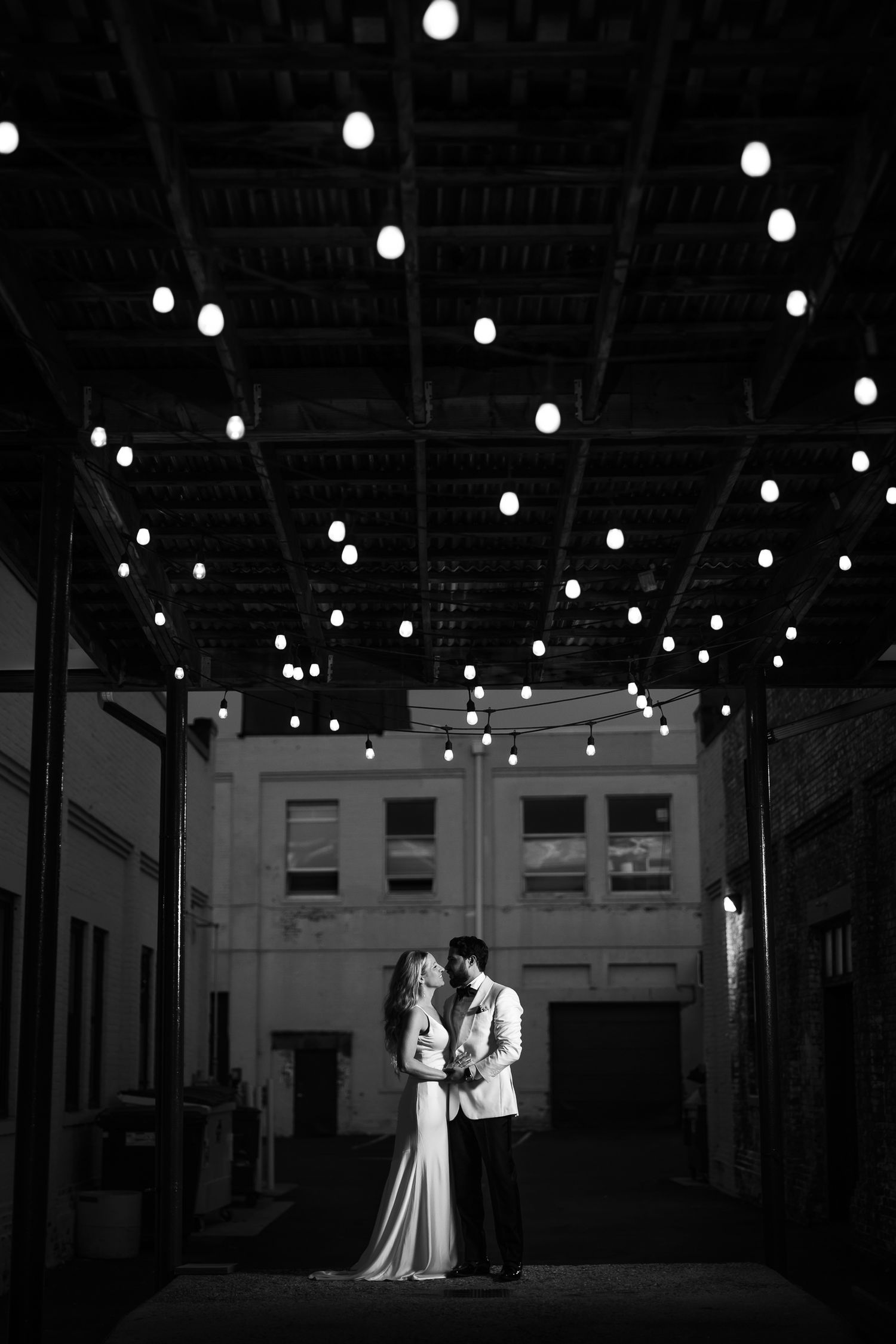 A black and white sequence showing silhouettes of a couple in a large industrial space with overhead lights.
