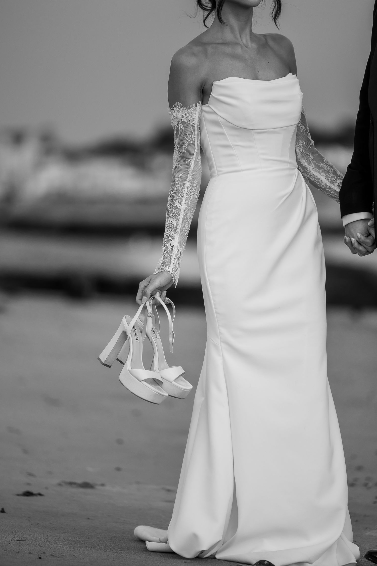 Close-up details of elegant white wedding dress and veil on sandy beach.