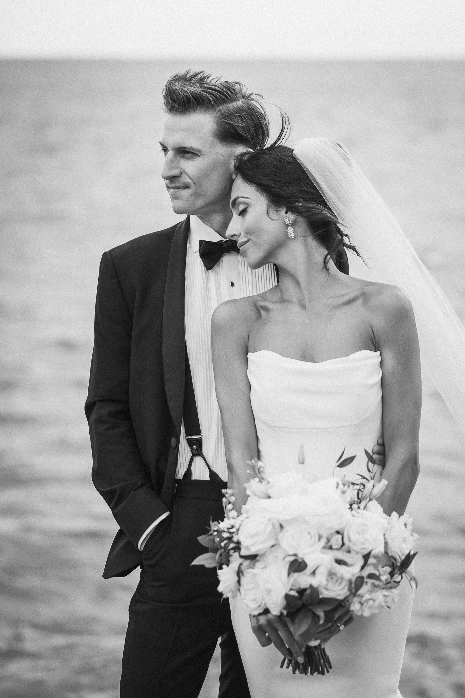 A bride and groom share intimate moments by the ocean in black and white.