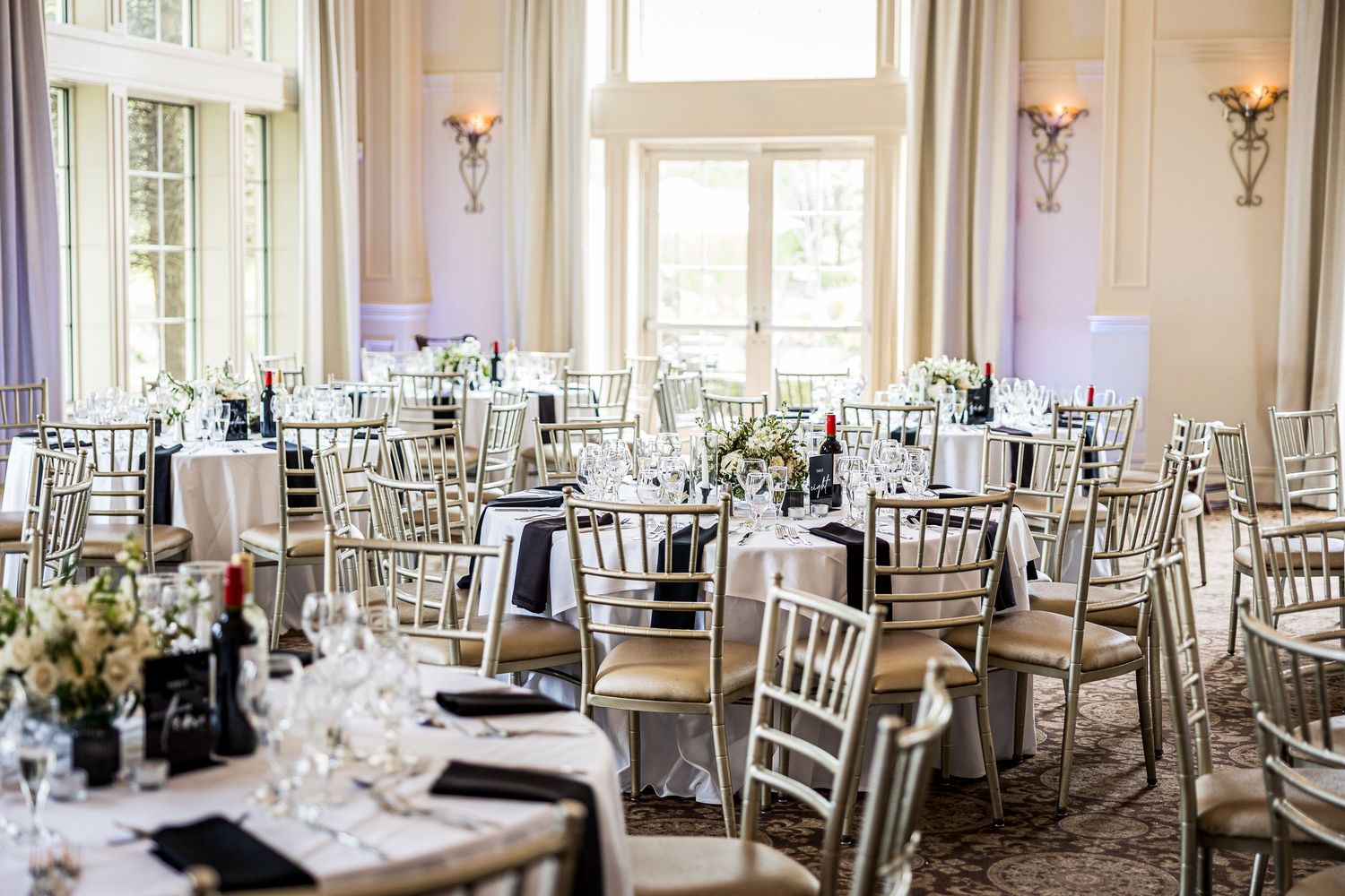 Elegant wedding reception hall set with white chiavari chairs and formal table settings.