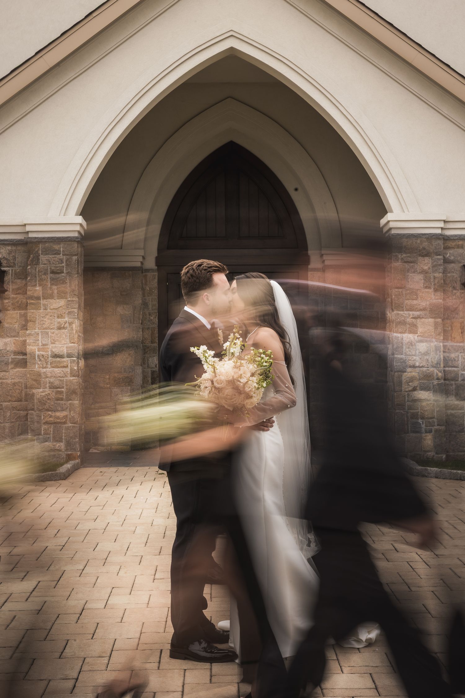 Motion blur captures dancing couple under stone archway during wedding celebration.