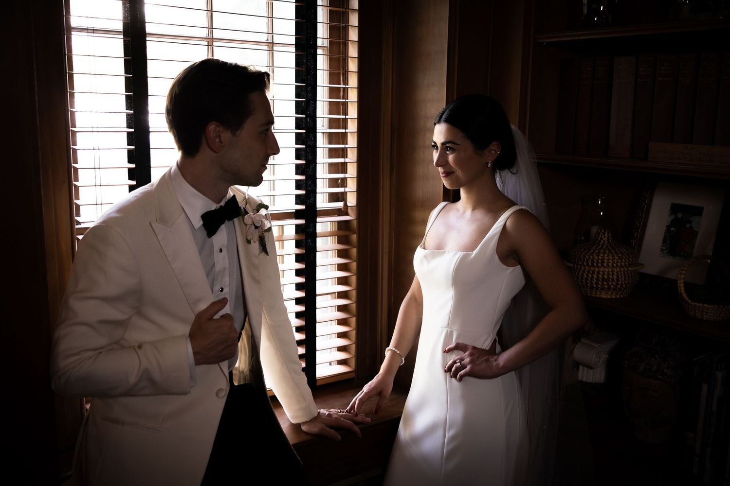 An intimate wedding moment captured in dramatic lighting through window blinds.