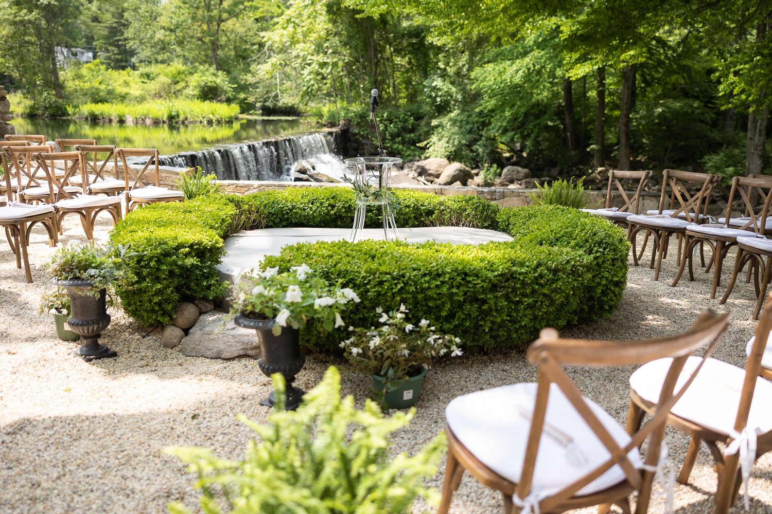 Lush garden wedding venue with green trees and water feature in background.