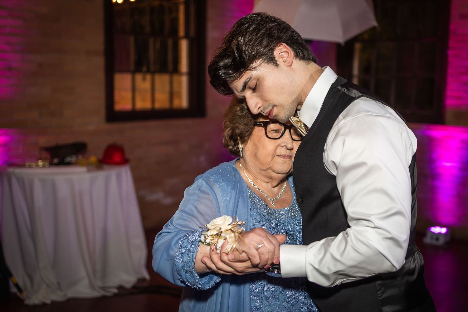 Wedding reception dance floor moment captured with pink ambient lighting.