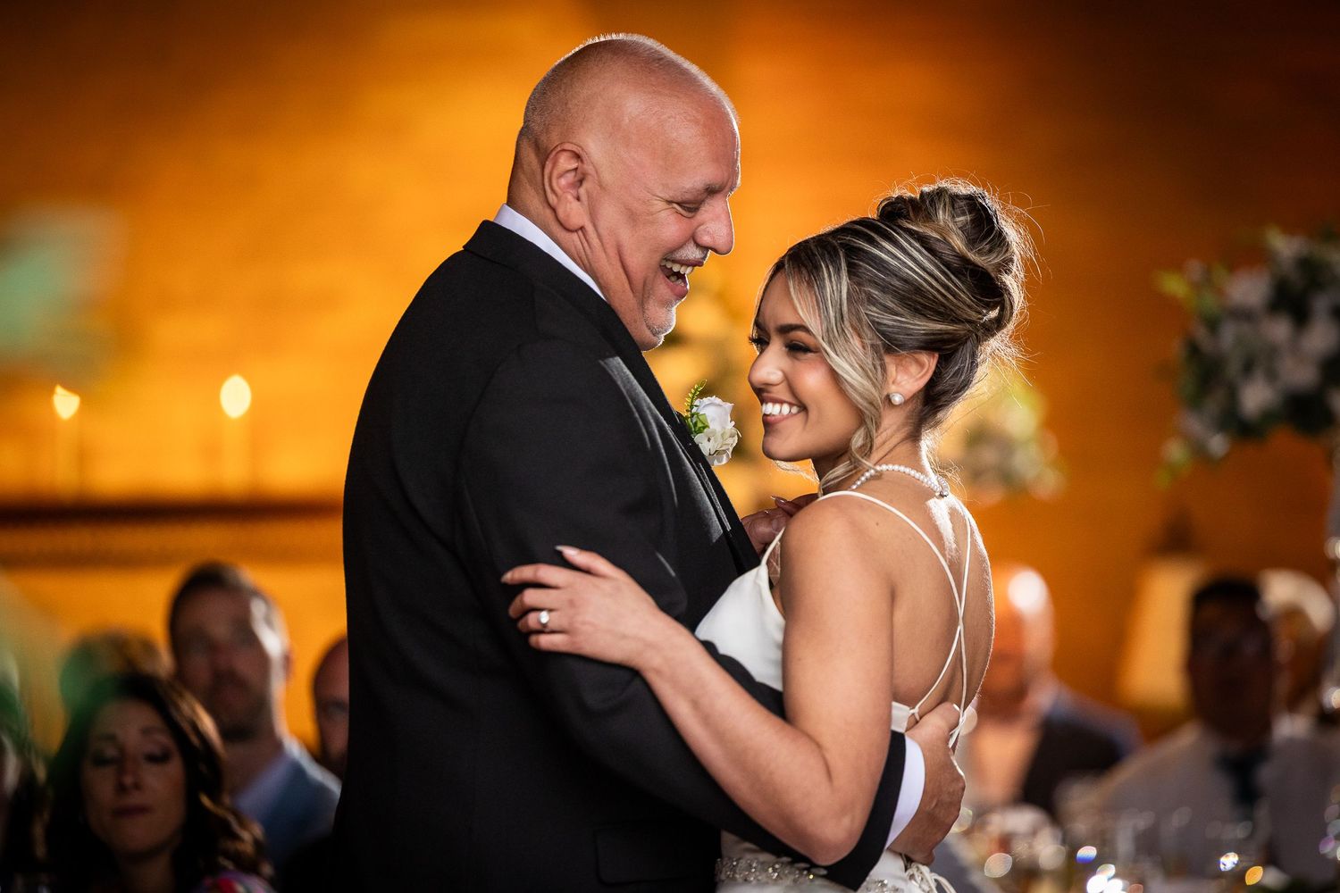 Romantic first dance at wedding reception with warm amber lighting and guests watching.