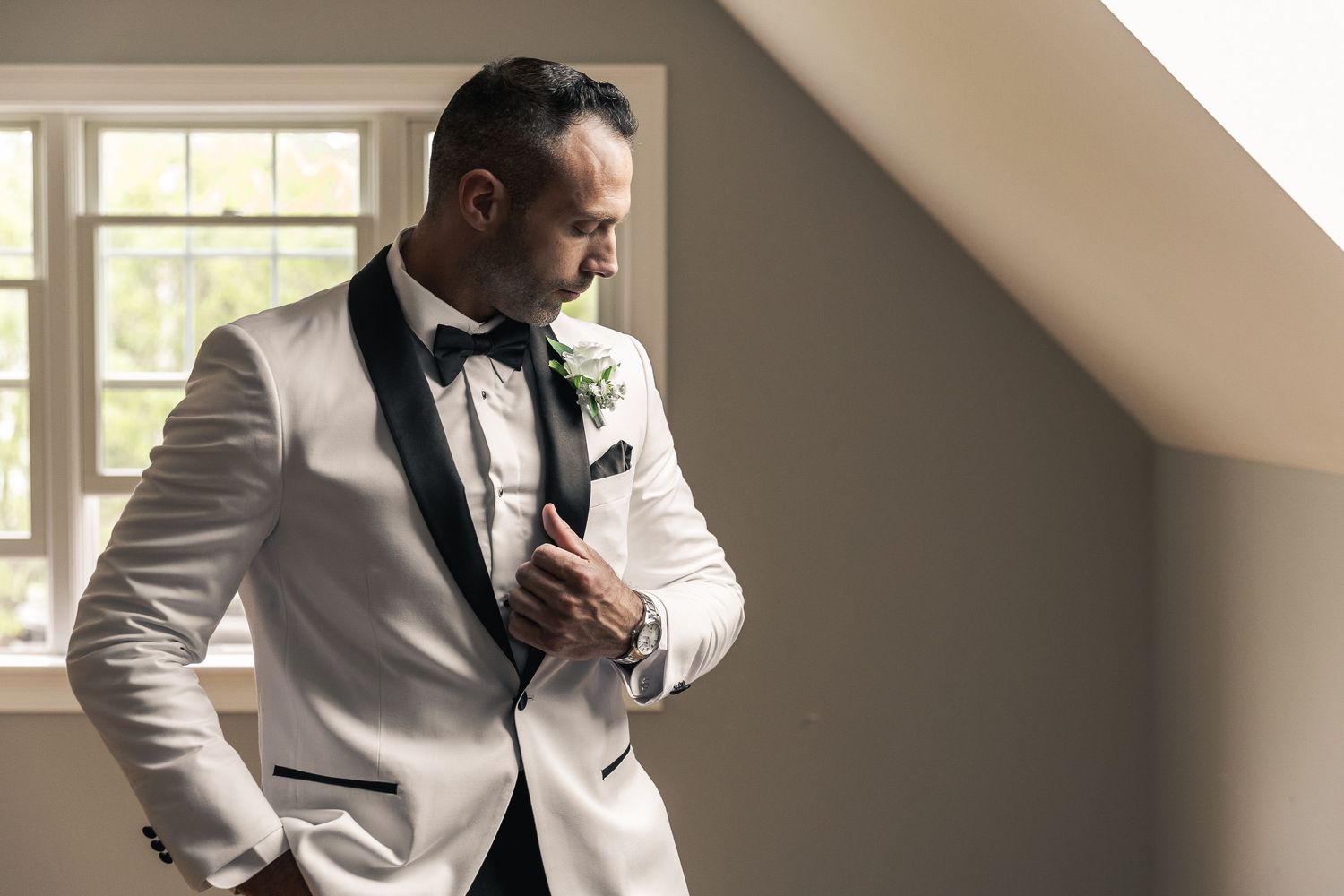 Groomsmen getting ready in formal attire by window with natural lighting.