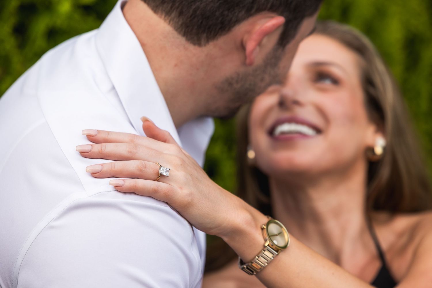 A joyful couple shares an intimate moment while laughing together outdoors in a garden setting.
