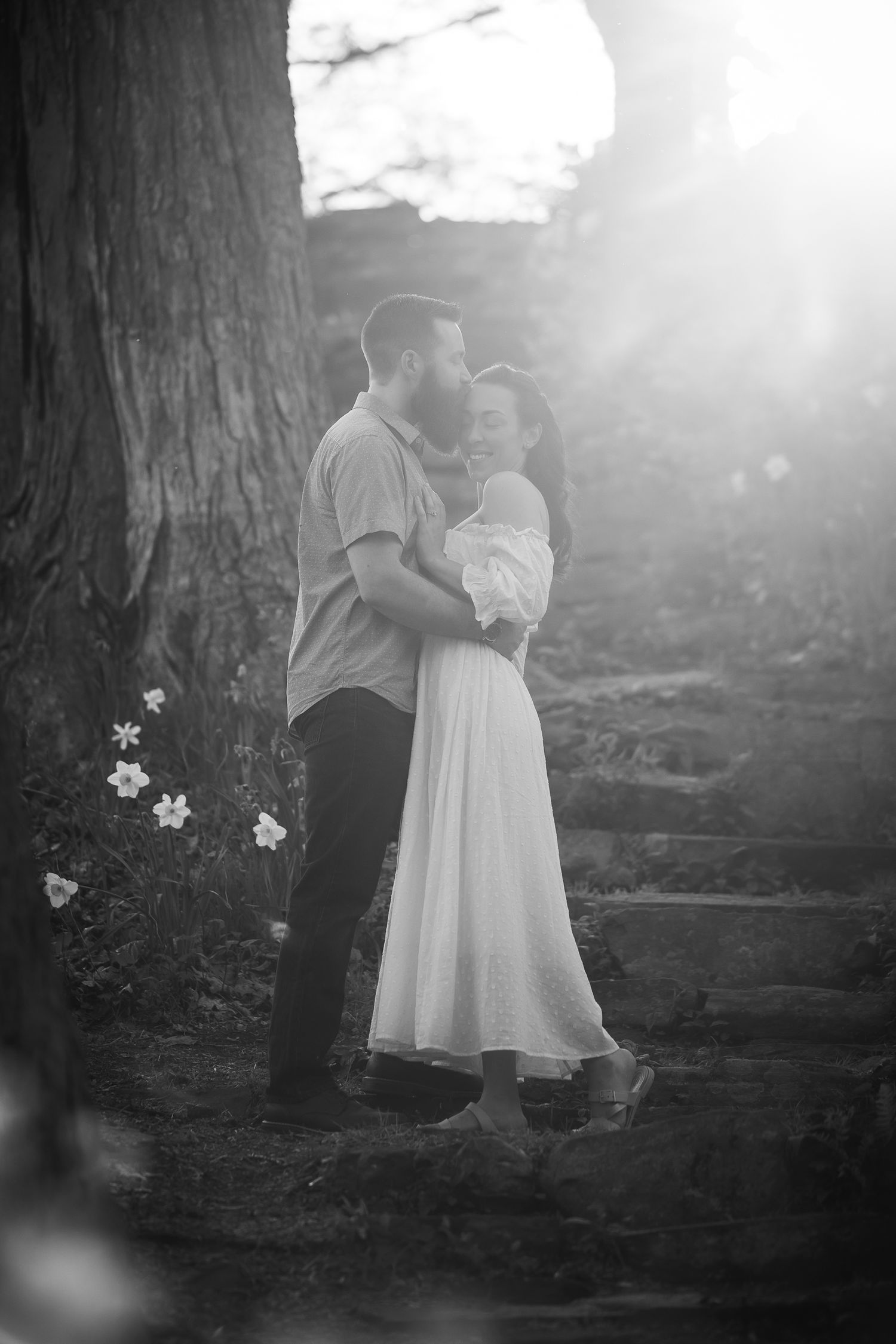 A dreamy black and white photo series of a couple in white clothing embracing under trees in a misty forest setting.