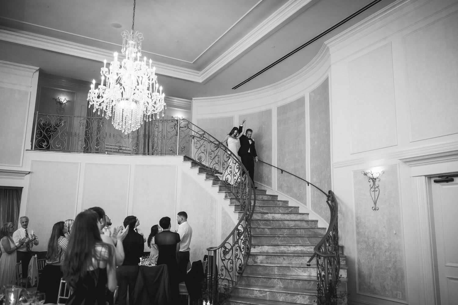 Black and white panorama of wedding reception in grand ballroom with crystal chandeliers.
