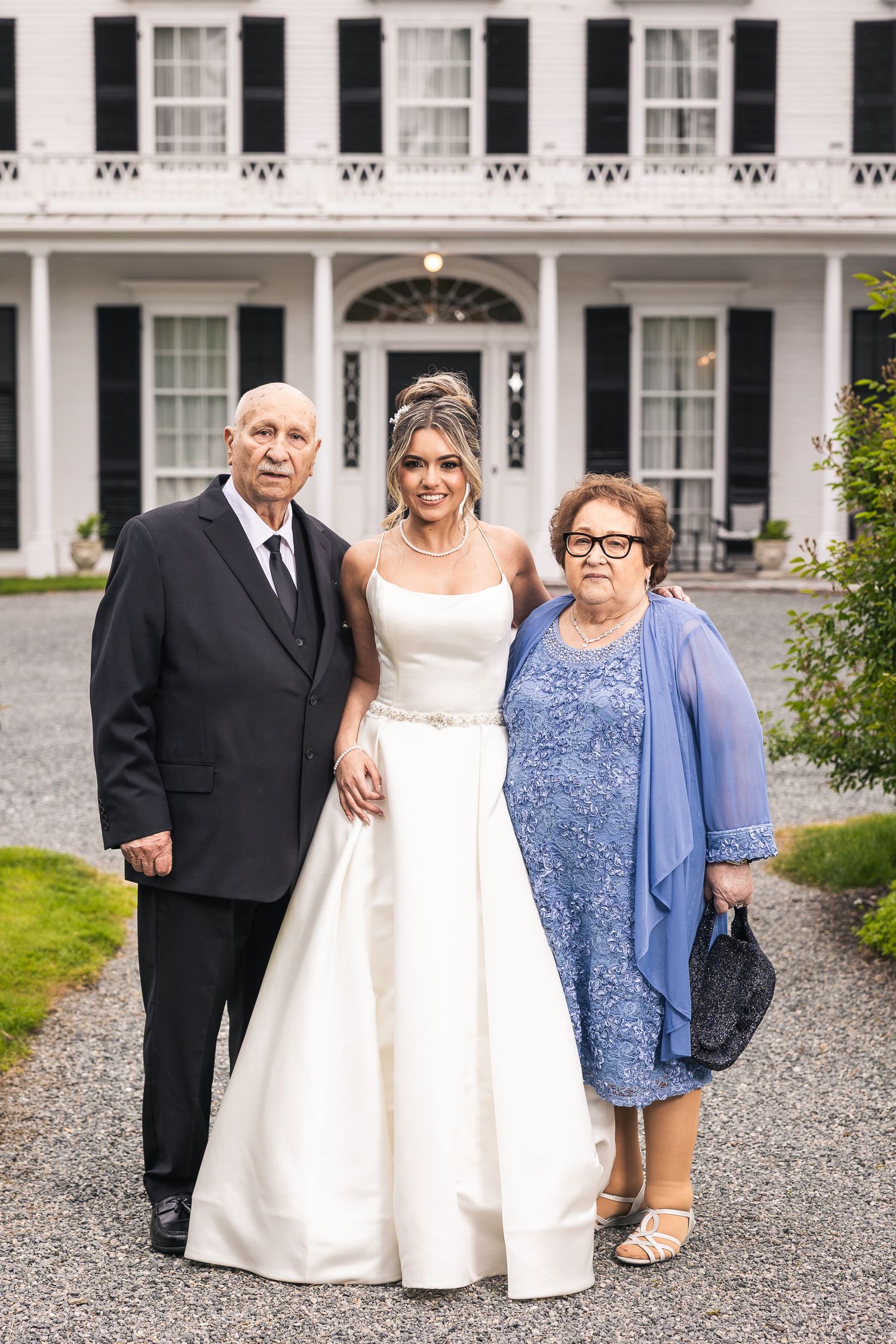 Family group portraits taken outside a stately white colonial mansion with black shutters.