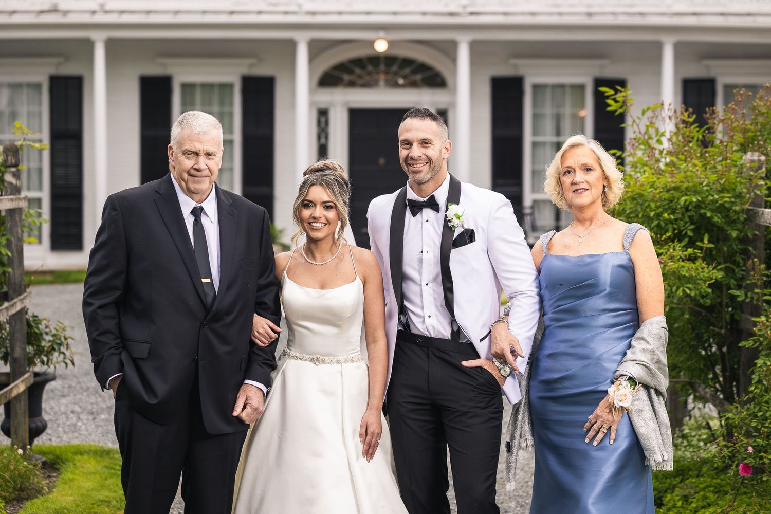 Wedding party members arranged in formal poses outside elegant white colonial estate.