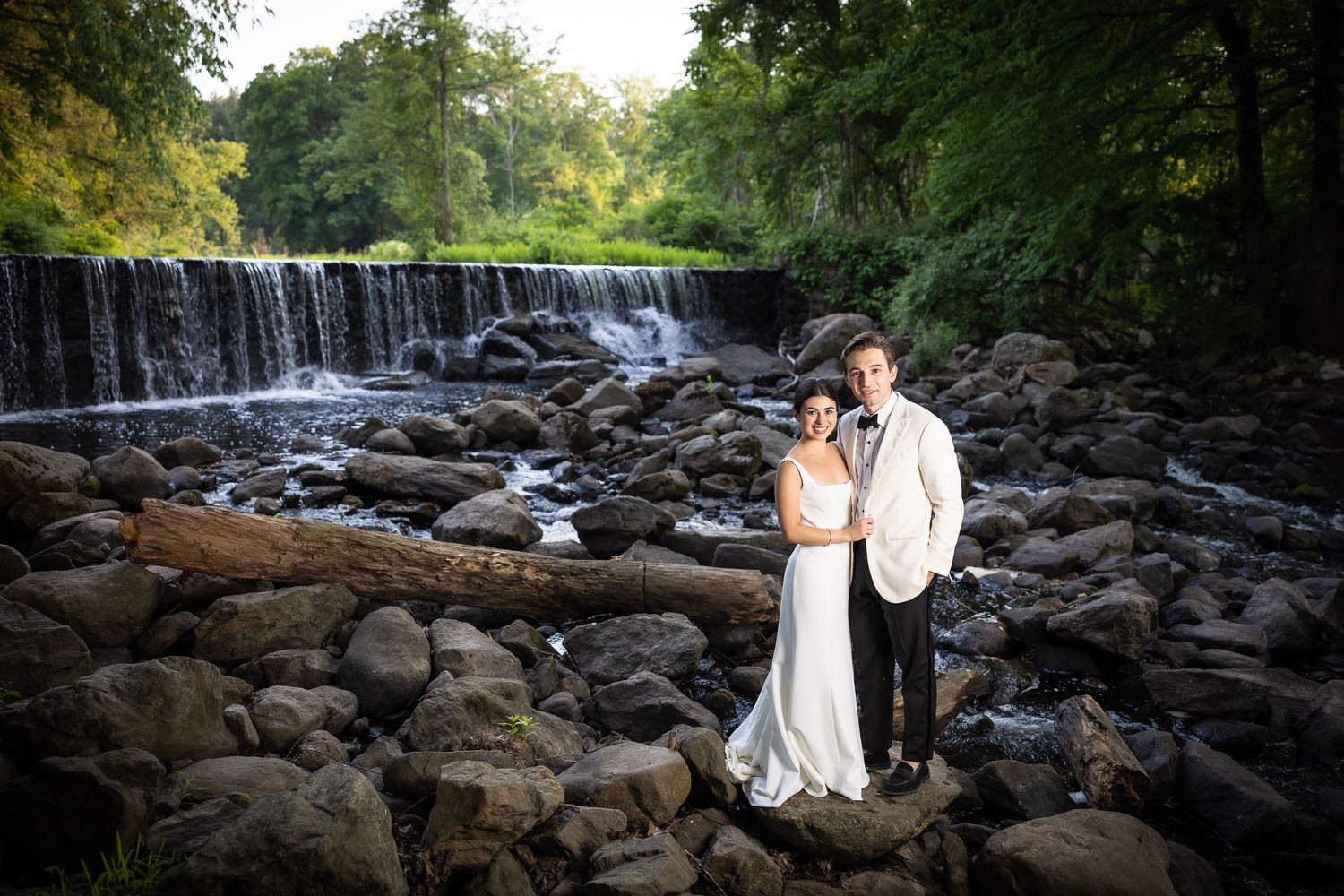 Newlyweds share an intimate moment by a scenic waterfall and rocky landscape.