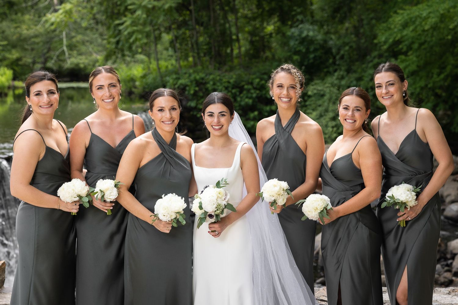 Wedding party in charcoal gray dresses and white bouquets posing outdoors.