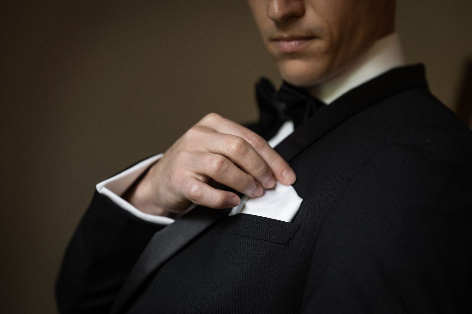 Close-up details of formal black tuxedo and bow tie adjustments.