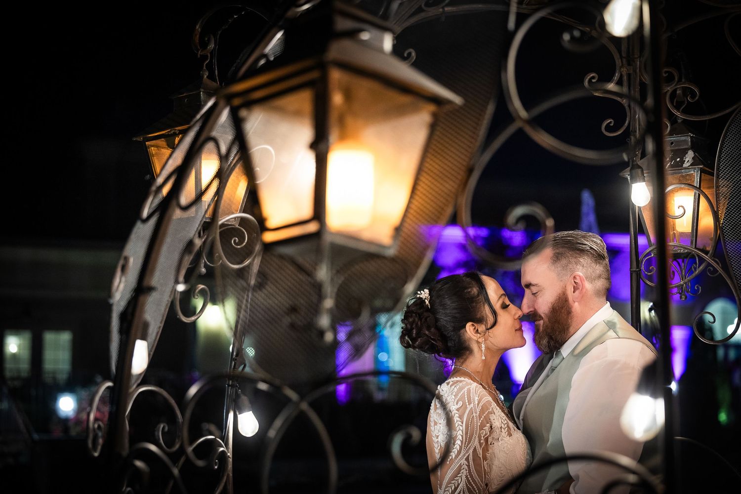 A romantic couple shares an intimate moment under a glowing vintage lantern at an evening outdoor celebration.