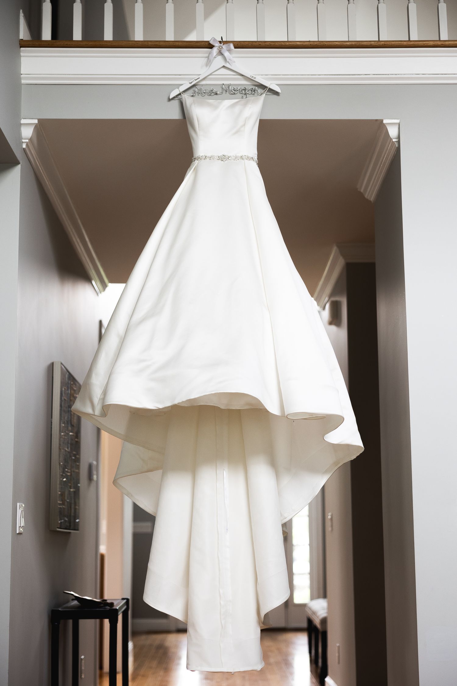 Multiple white wedding dresses hanging in a row against white interior walls.