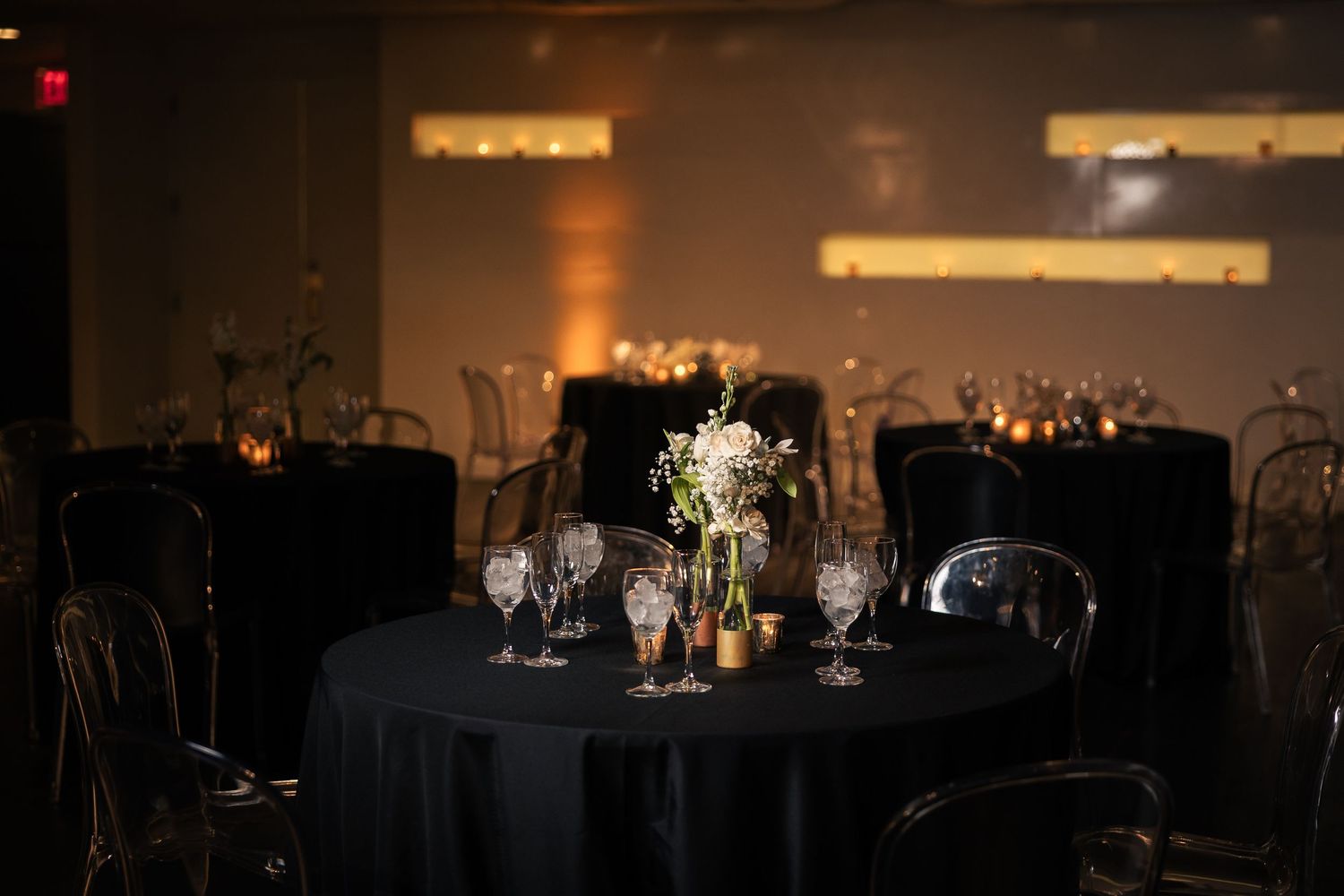 Elegant wedding reception tables with black linens and white floral centerpieces in a dimly lit ballroom.