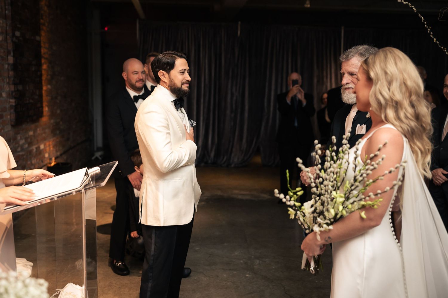 A couple shares their first dance as newlyweds in a dimly lit reception venue with romantic lighting and decor.