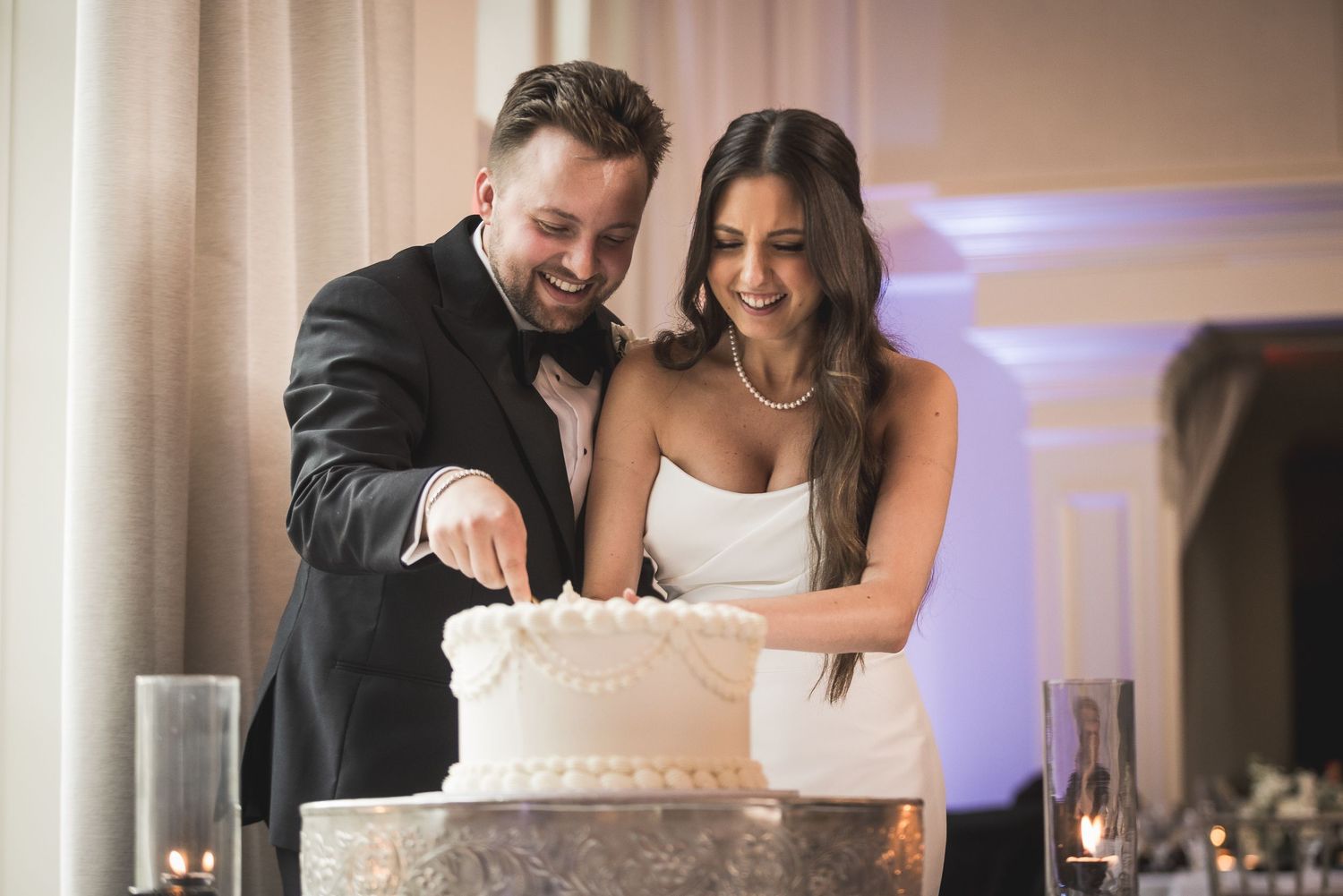 Couple cuts their wedding cake together at reception under soft lighting.