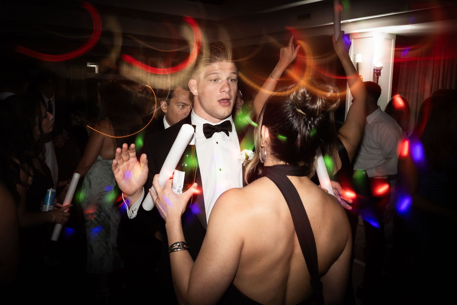 Wedding guests dance and celebrate on a dimly lit dance floor during an evening reception.