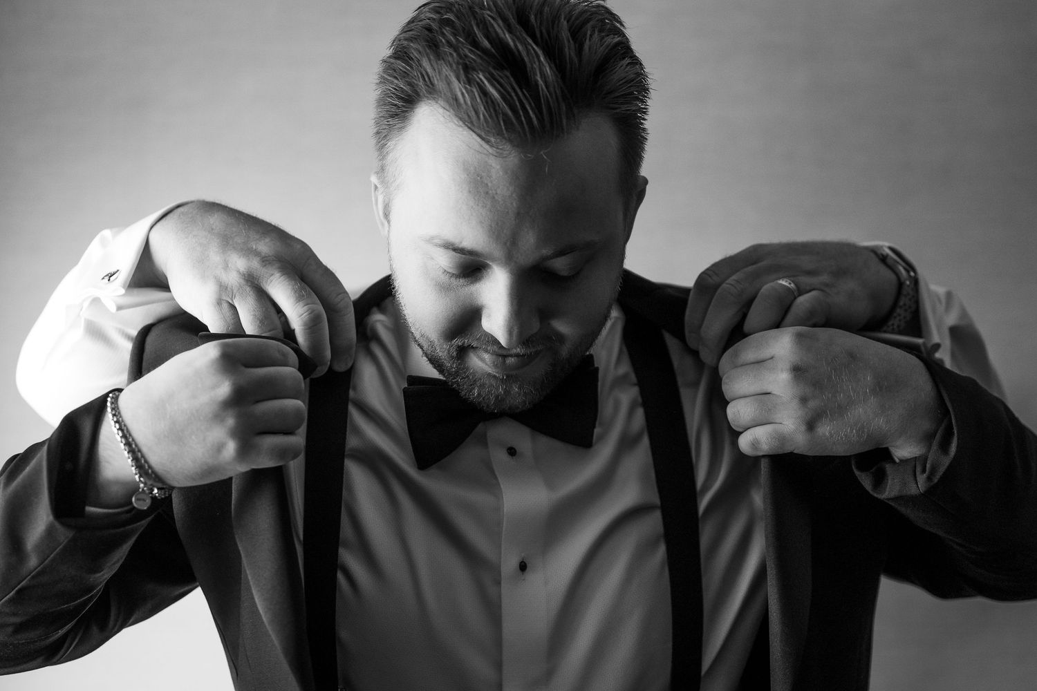 A black and white sequence of someone putting on a formal suit jacket and adjusting the collar.
