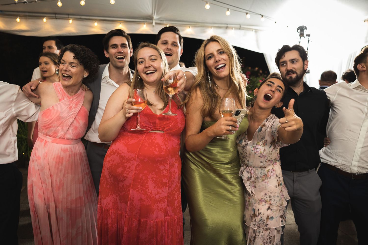Wedding guests in pink and floral dresses posing together at a wedding reception.
